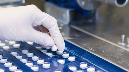 Gloved hand placing white tablets in blue blisters